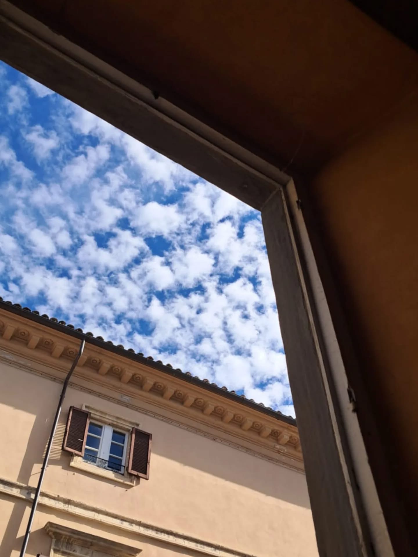 finestra cielo Vista da un interno verso il cielo azzurro con nuvole bianche, inquadrato da una cornice scura e da una facciata in pietra