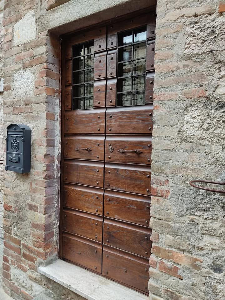 portone Porta in legno scuro con pannelli orizzontali e finestra superiore a grata, inserita in muro di mattoni rossi e pietra.