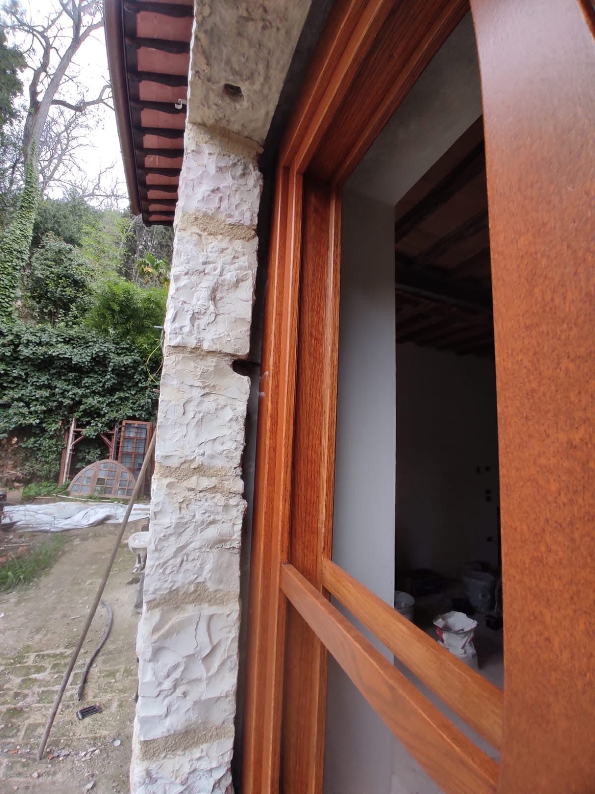 telaio finestra Finestra in legno scuro su parete in pietra chiara, con giardino e vegetazione sullo sfondo.